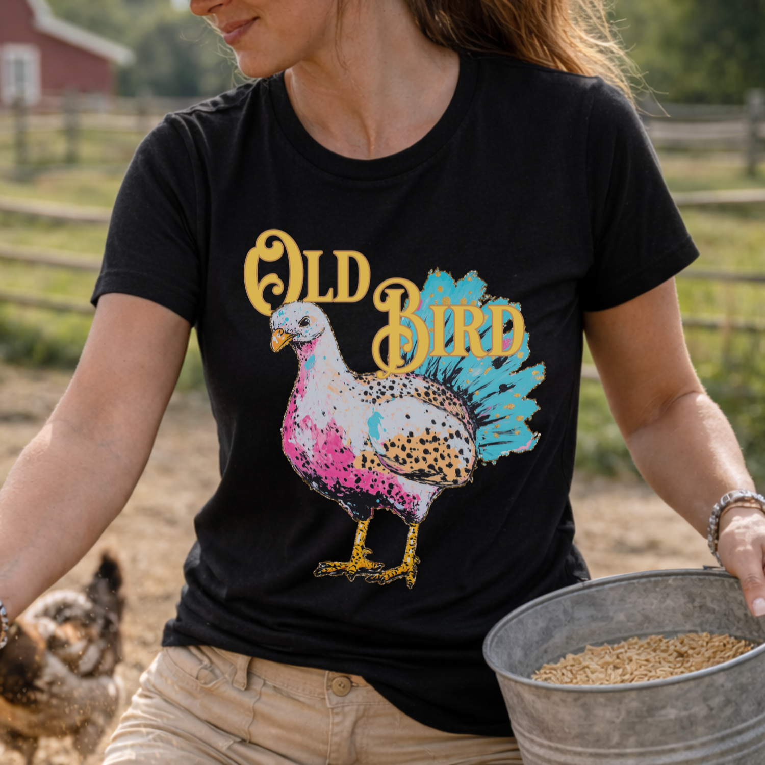 Person wearing a black t-shirt with 'Old Bird' graphic design, holding a bucket of seeds on a farm.