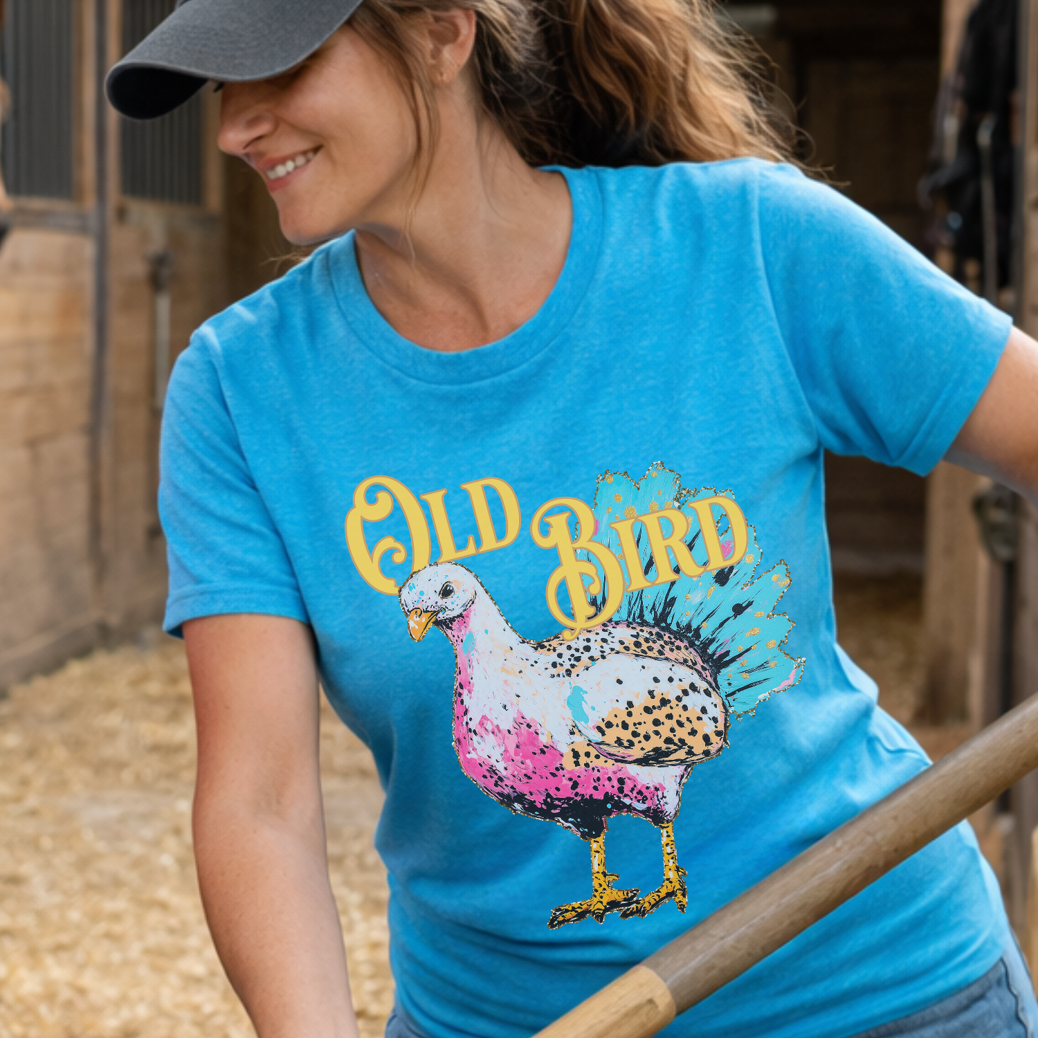 Person wearing a blue t-shirt with a colorful bird graphic and 'Old Bird' text, standing in a barn.