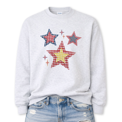 Patriotic patchwork star graphic on a gray sweatshirt. The design features a cluster of illustrated stars in varied sizes, each filled with classic red, white, and blue gingham-style patterns, including plaid and check textures. Small accent sparkles add movement while the layered patchwork look gives the graphic a cozy, Americana feel. A versatile patriotic design ideal for Fourth of July, summer events, and seasonal USA collections.
