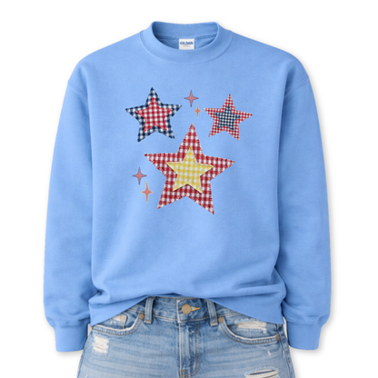 Patriotic patchwork star graphic on a blue sweatshirt. The design features a cluster of illustrated stars in varied sizes, each filled with classic red, white, and blue gingham-style patterns, including plaid and check textures. Small accent sparkles add movement while the layered patchwork look gives the graphic a cozy, Americana feel. A versatile patriotic design ideal for Fourth of July, summer events, and seasonal USA collections.