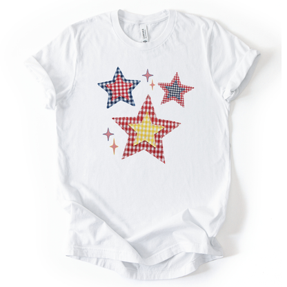 Patriotic Americana star graphic on a white t-shirt. The design features illustrated patchwork stars arranged in a playful cluster, using red, white, and blue gingham-style patterns with subtle texture and stitching detail. Small accent stars add movement and balance around the main shapes. The overall look feels classic, cheerful, and vintage-inspired, making it ideal for Fourth of July, summer Americana collections, and everyday patriotic wear.