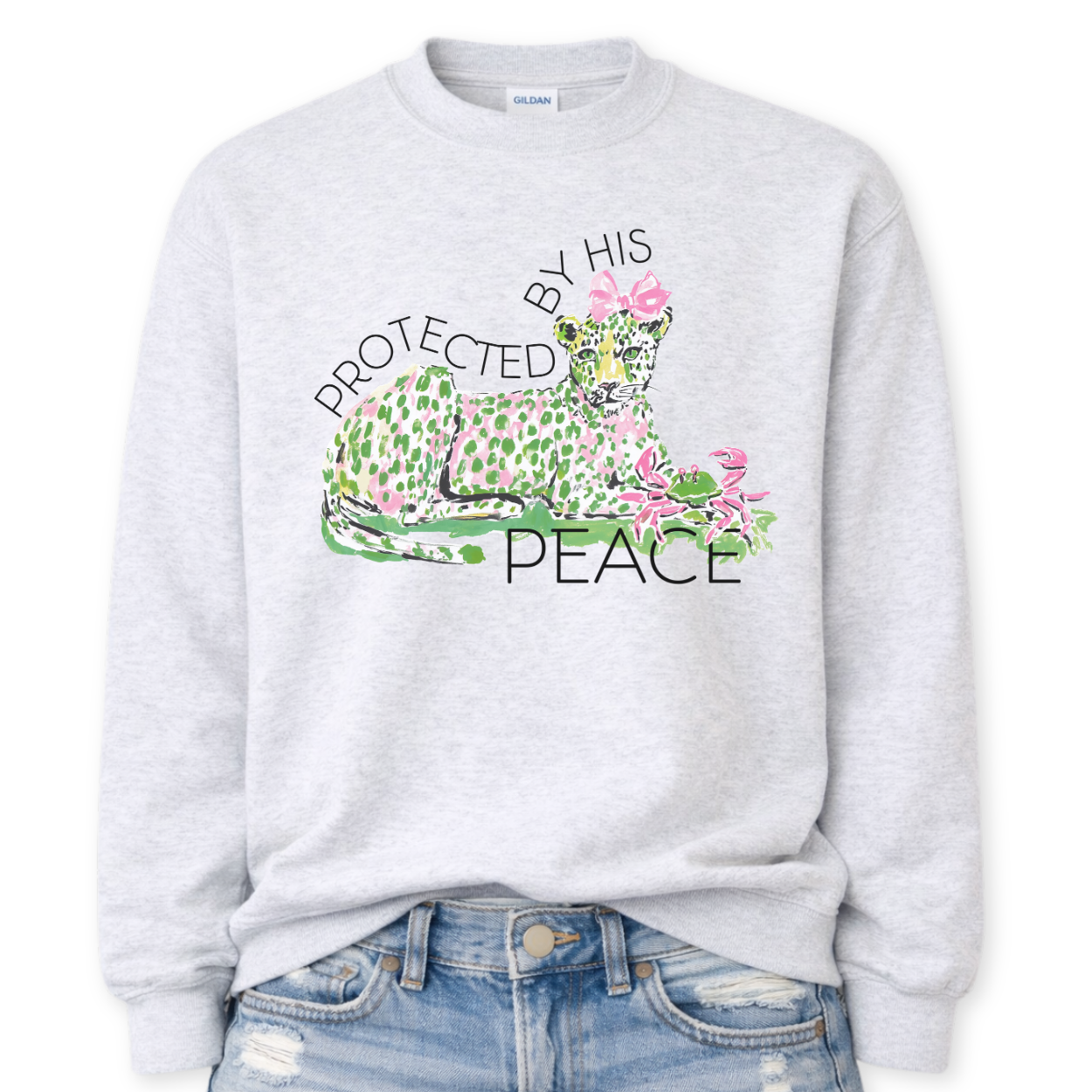 Ash Gray Bold Christian Easter graphic on a Gildan crewneck sweatshirt. The design features a reclining leopard illustrated in soft pink and green tones with a coordinating bow, paired with the phrase “Protected By His Peace” in a clean, modern layout. The artwork blends feminine spring colors with a strong faith message