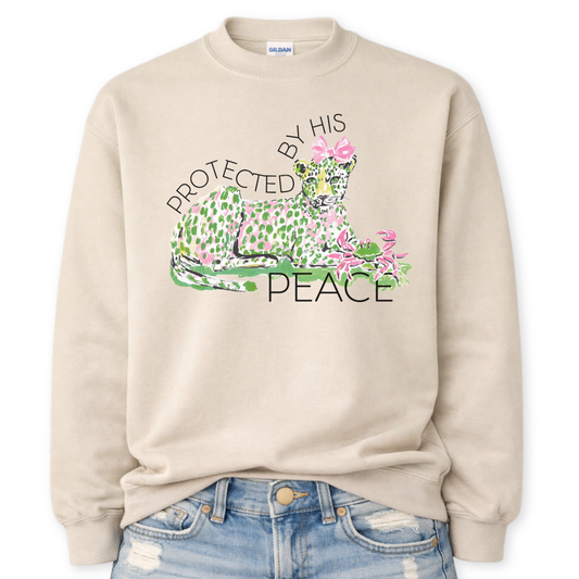 Beige Bold Christian Easter graphic on a Gildan crewneck sweatshirt. The design features a reclining leopard illustrated in soft pink and green tones with a coordinating bow, paired with the phrase “Protected By His Peace” in a clean, modern layout. The artwork blends feminine spring colors with a strong faith message