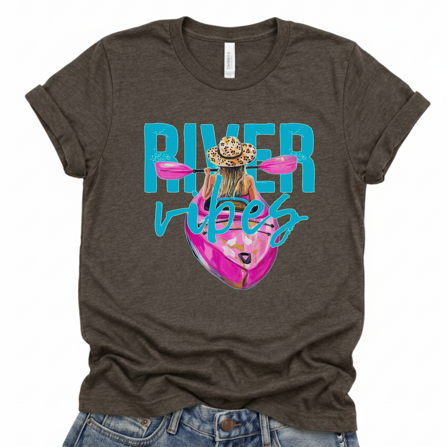 River Vibes kayak graphic on a soft unisex Bella Canvas dark heather gray t shirt. The artwork shows a woman paddling a kayak from a back view wearing a leopard print sun hat, with pink paddles stretching across the top of the design.