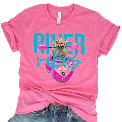 River Vibes kayak graphic on a soft unisex Bella Canvas heather charity pink  t shirt. The artwork shows a woman paddling a kayak from a back view wearing a leopard print sun hat, with pink paddles stretching across the top of the design.