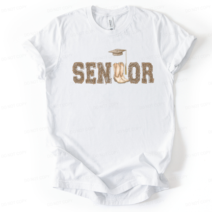 Graduation western themed graphic t shirt. The design features the word Senior in rustic western lettering with cowboy boots forming the center detail, topped with a graduation cap and tassel. 
