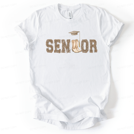 Graduation western themed graphic t shirt. The design features the word Senior in rustic western lettering with cowboy boots forming the center detail, topped with a graduation cap and tassel. 