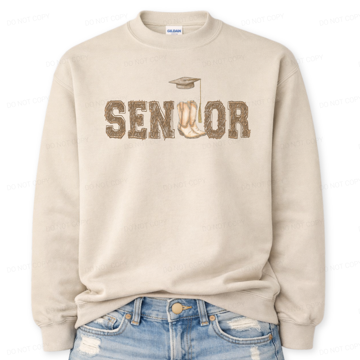 Western graduation graphic on a classic sand crewneck sweatshirt. The design features SENIOR in bold varsity style lettering with a pair of cowboy boots integrated into the wordmark and a small graduation cap detail above,