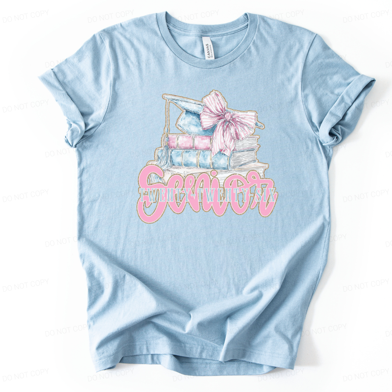 Graduation 2026 academic themed graphic t shirt. The design features a stacked book illustration topped with a light blue graduation cap and tassel, accented with a large pink bow. The front reads Senior with Twenty Twenty Six layered underneath, creating a preppy graduation look 