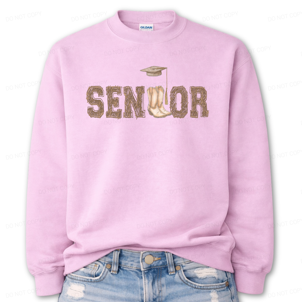 Western graduation graphic on a classic pink crewneck sweatshirt. The design features SENIOR in bold varsity style lettering with a pair of cowboy boots integrated into the wordmark and a small graduation cap detail above,