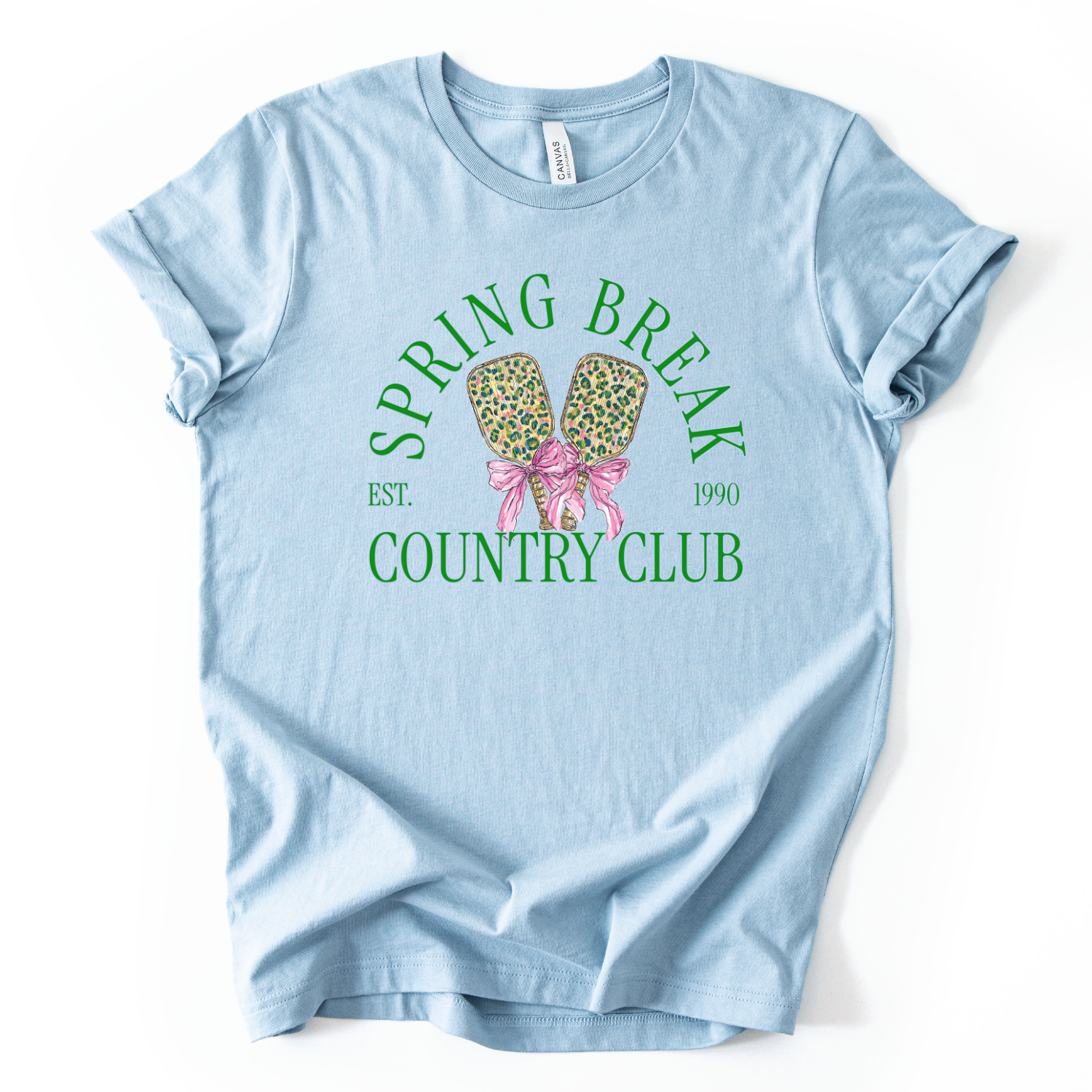 blue t-shirt with 'Spring Break Country Club' graphic on a white background.The trending graphic features a pair of illustrated pickleball paddles with a leopard-style pattern, tied together with a pink ribbon bow at the center. Arched text reads “Spring Break Country Club”, with small accent text adding a vintage-inspired touch. The overall design feels playful, preppy, and spring-ready.
