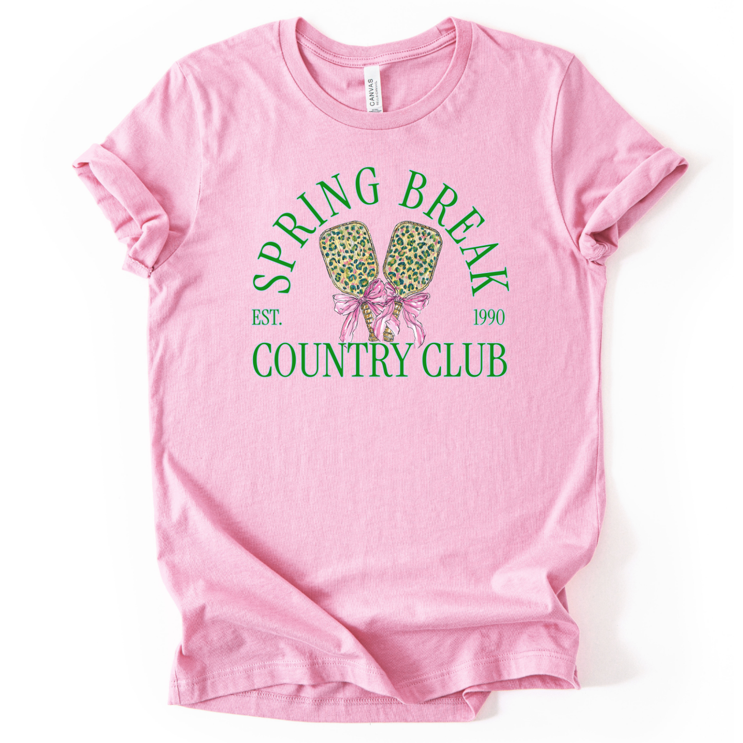pink t-shirt with 'Spring Break Country Club' graphic on a white background.The trending graphic features a pair of illustrated pickleball paddles with a leopard-style pattern, tied together with a pink ribbon bow at the center. Arched text reads “Spring Break Country Club”, with small accent text adding a vintage-inspired touch. The overall design feels playful, preppy, and spring-ready.