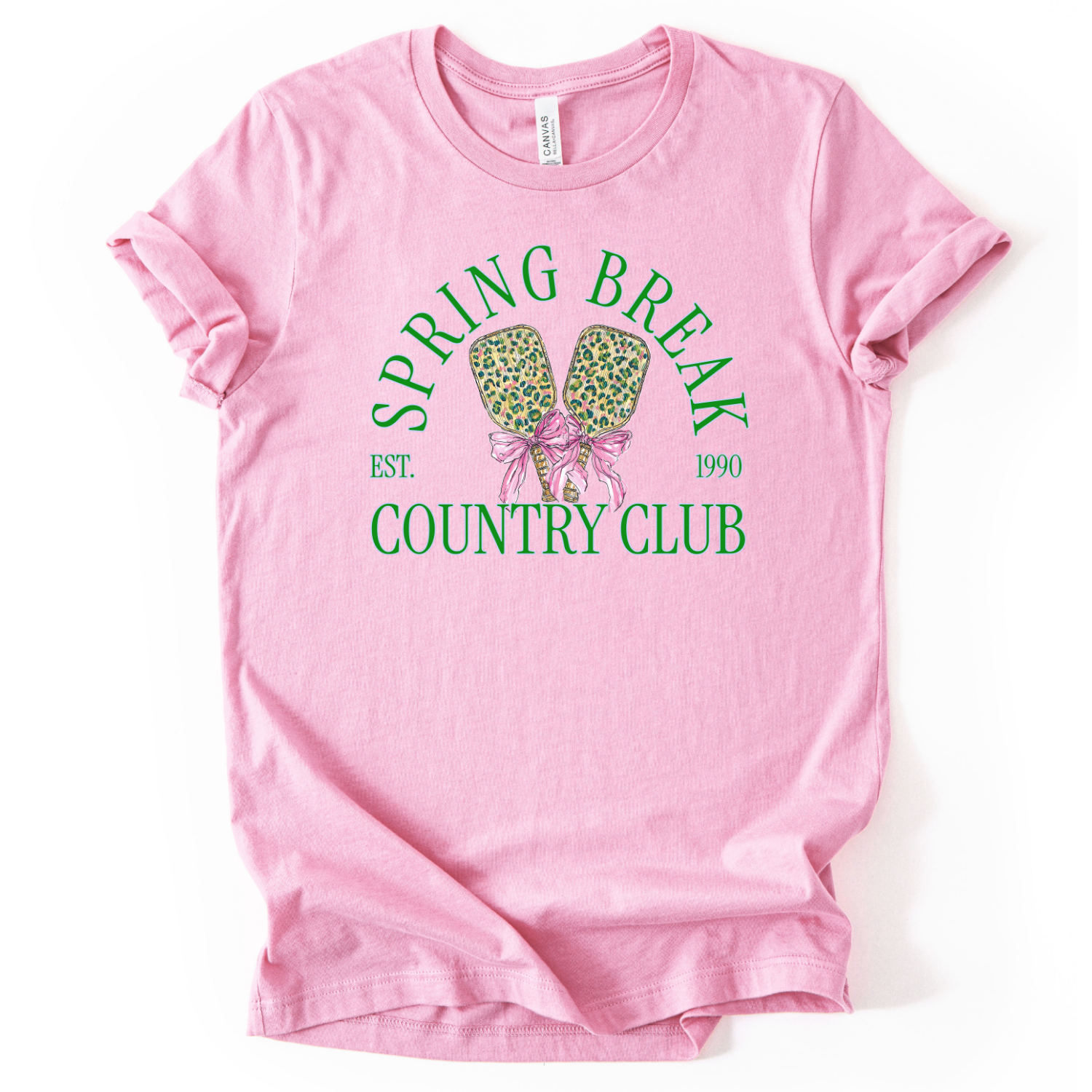 pink t-shirt with 'Spring Break Country Club' graphic on a white background.The trending graphic features a pair of illustrated pickleball paddles with a leopard-style pattern, tied together with a pink ribbon bow at the center. Arched text reads “Spring Break Country Club”, with small accent text adding a vintage-inspired touch. The overall design feels playful, preppy, and spring-ready.