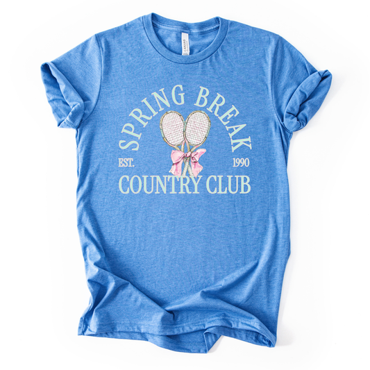 Blue t-shirt with 'Spring Break Country Club' text and graphics on a white background.The graphic features a pair of illustrated tennis rackets crossed at the handles and tied together with a soft pink ribbon bow at the center. Arched text reads “Spring Break Country Club”, with small accent details adding a classic, collegiate feel. 