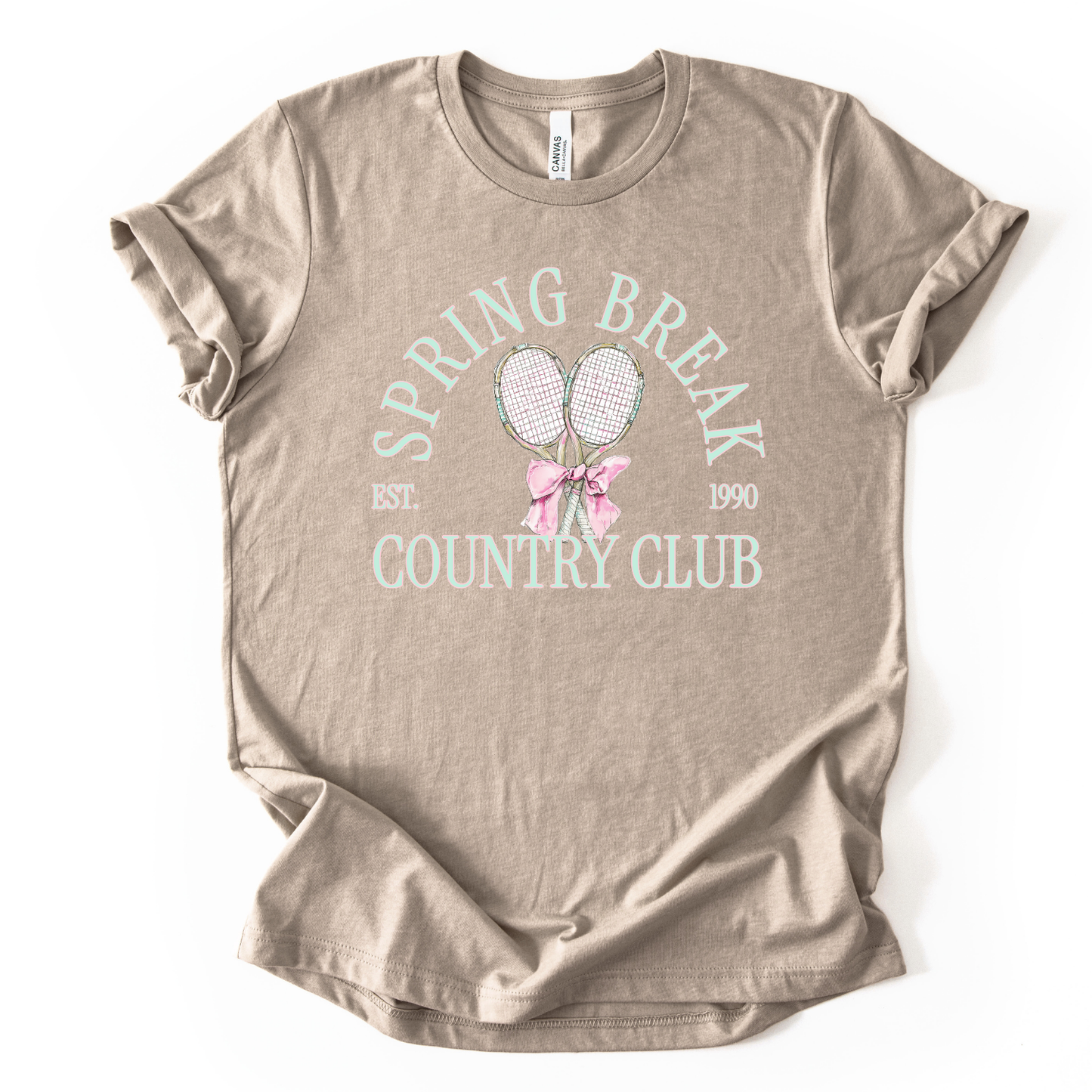 tan t-shirt with 'Spring Break Country Club' text and graphics on a white background.The graphic features a pair of illustrated tennis rackets crossed at the handles and tied together with a soft pink ribbon bow at the center. Arched text reads “Spring Break Country Club”, with small accent details adding a classic, collegiate feel. 