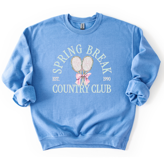Blue Preppy spring tennis country club graphic on a sweatshirt. The graphic features the phrase “Spring Break Country Club” in arched collegiate lettering, with small “EST.” and “1990” accents on each side. Two illustrated tennis racquets are centered beneath the text and tied together with a soft pink bow, creating a polished yet playful design that blends sporty charm with spring color appeal. 
