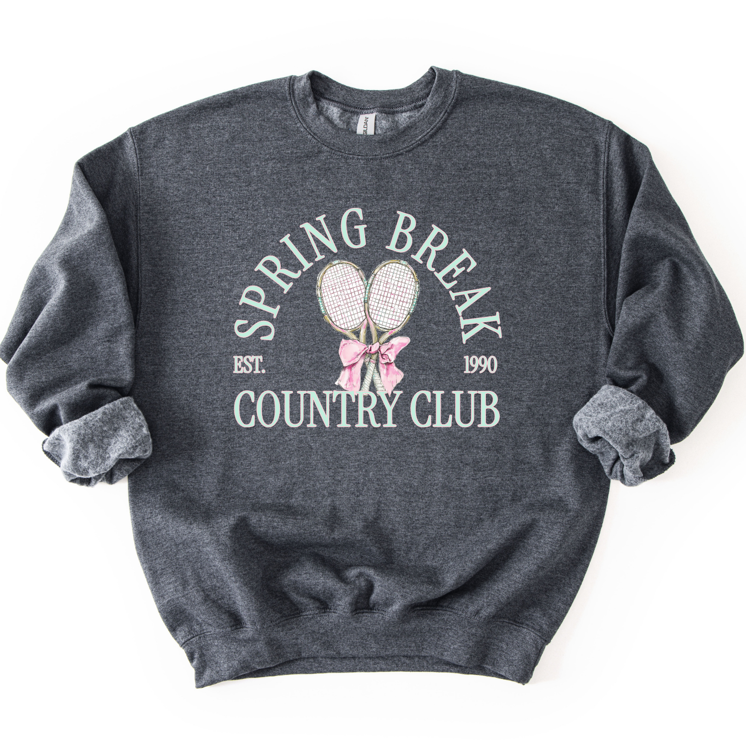 Gray Preppy spring tennis country club graphic on a sweatshirt. The graphic features the phrase “Spring Break Country Club” in arched collegiate lettering, with small “EST.” and “1990” accents on each side. Two illustrated tennis racquets are centered beneath the text and tied together with a soft pink bow, creating a polished yet playful design that blends sporty charm with spring color appeal. 