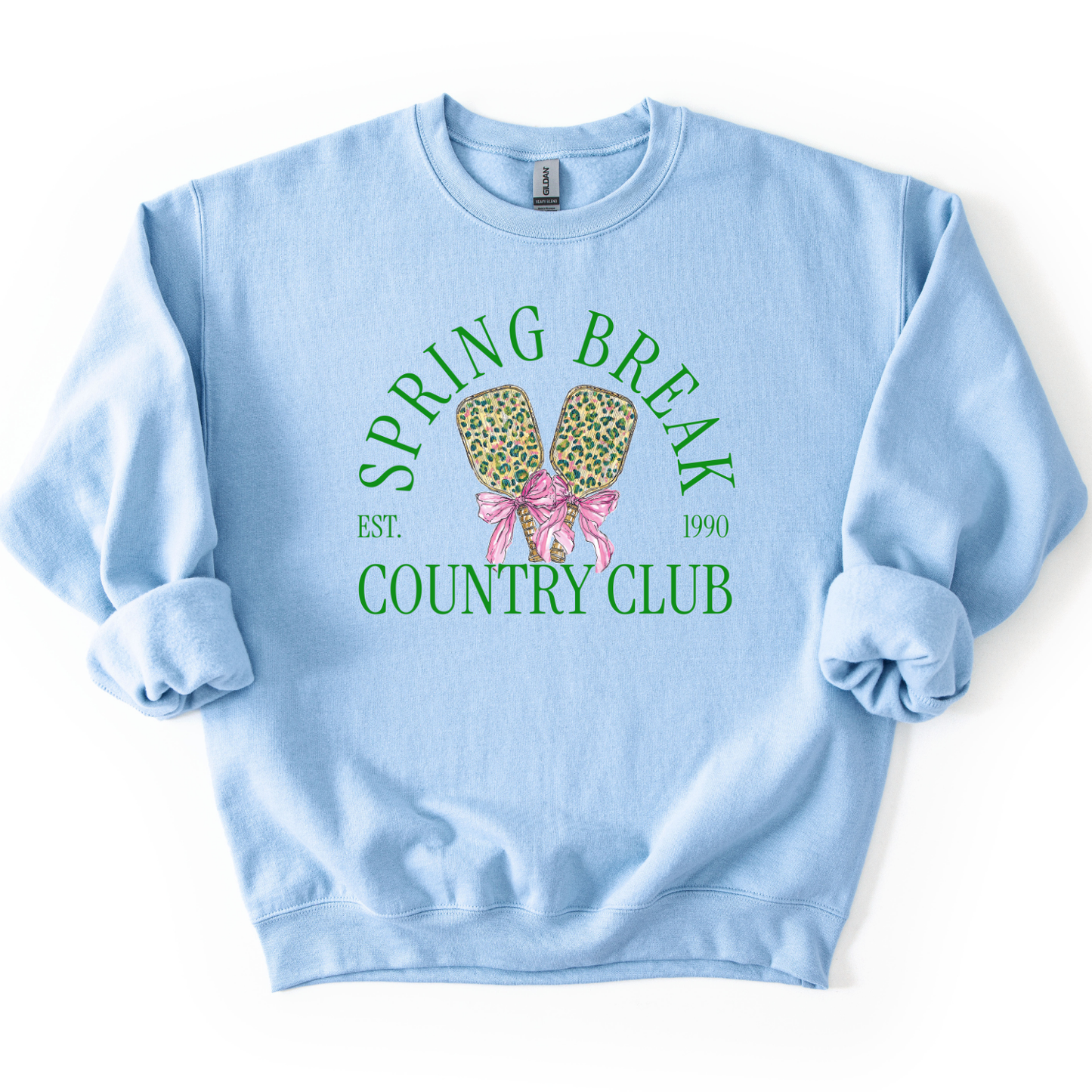 Preppy spring pickleball country club graphic on a sweatshirt. The graphic features the phrase “Spring Break Country Club” in arched collegiate lettering, with small “EST.” and “1990” accents on each side. Two illustrated pickleball paddles sit centered beneath the text and are tied together with a pink bow, creating a playful, sporty-coastal look that fits spring floor sets, pickleball gift sections, and casual lifestyle apparel displays.