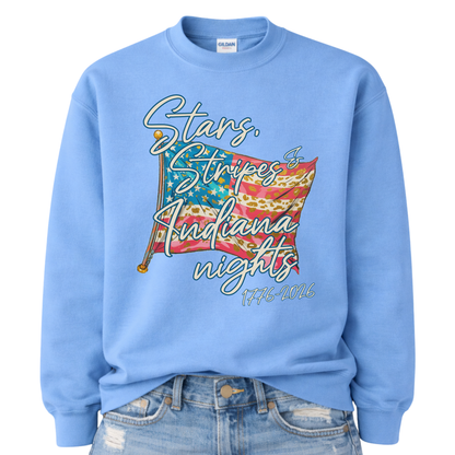 Patriotic stars and stripes graphic on a blue sweatshirt. The artwork shows a waving American flag with stars, striped details, and leopard-print accents, paired with script lettering that reads “Stars, Stripes & ___ Nights” plus “1776–2026” for a bold Fourth of July and summer patriotic look. Customizable location option: add any City or State (up to 30 characters) to make it a hometown, vacation spot, or event-ready USA piece.