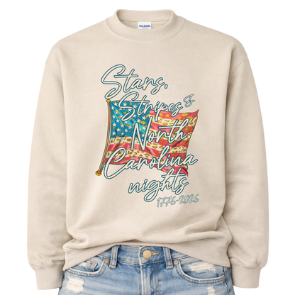 Patriotic stars and stripes graphic on a tan sweatshirt. The artwork shows a waving American flag with stars, striped details, and leopard-print accents, paired with script lettering that reads “Stars, Stripes & ___ Nights” plus “1776–2026” for a bold Fourth of July and summer patriotic look. Customizable location option: add any City or State (up to 30 characters) to make it a hometown, vacation spot, or event-ready USA piece.