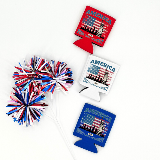Assorted patriotic collapsible can coolers in red, white, and royal blue featuring a Statue of Liberty and American flag graphic with the wording “America Sweet Land of Liberty 1776,” styled with red, white, and blue pom poms on a white background.