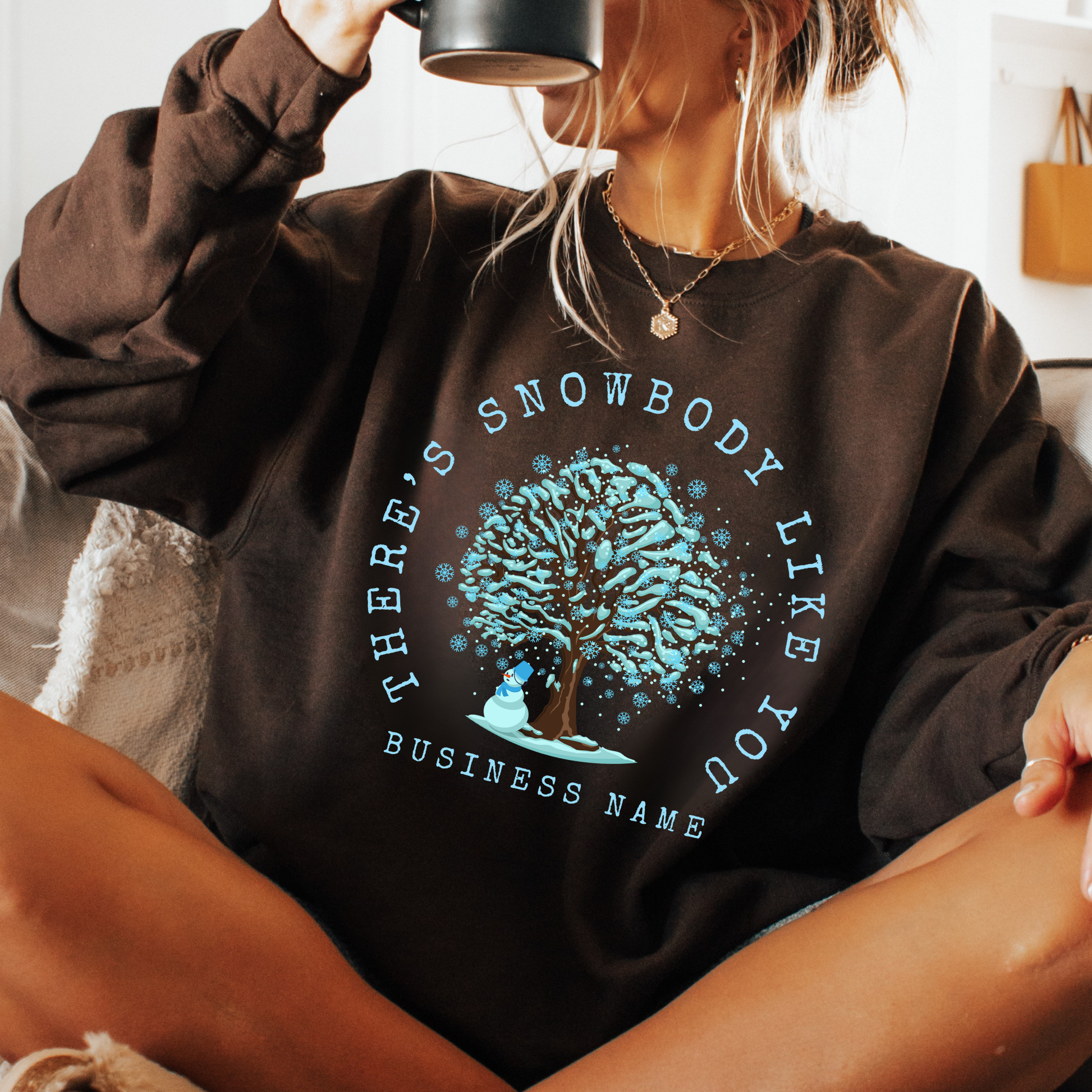 There's snowbody like you text wrapped around a tree with branches full of blue snow and a snowman underneath.  customize with business name, city or town or both.  brown sweatshirt