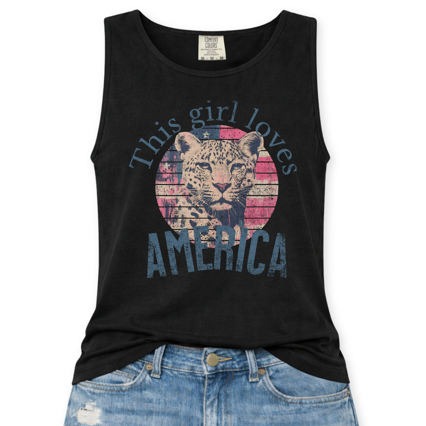 Black Comfort Colors tank top featuring a vintage-style patriotic graphic with a leopard illustration inside a distressed American flag circle and the phrase “This Girl Loves America,” styled with light wash denim jeans.