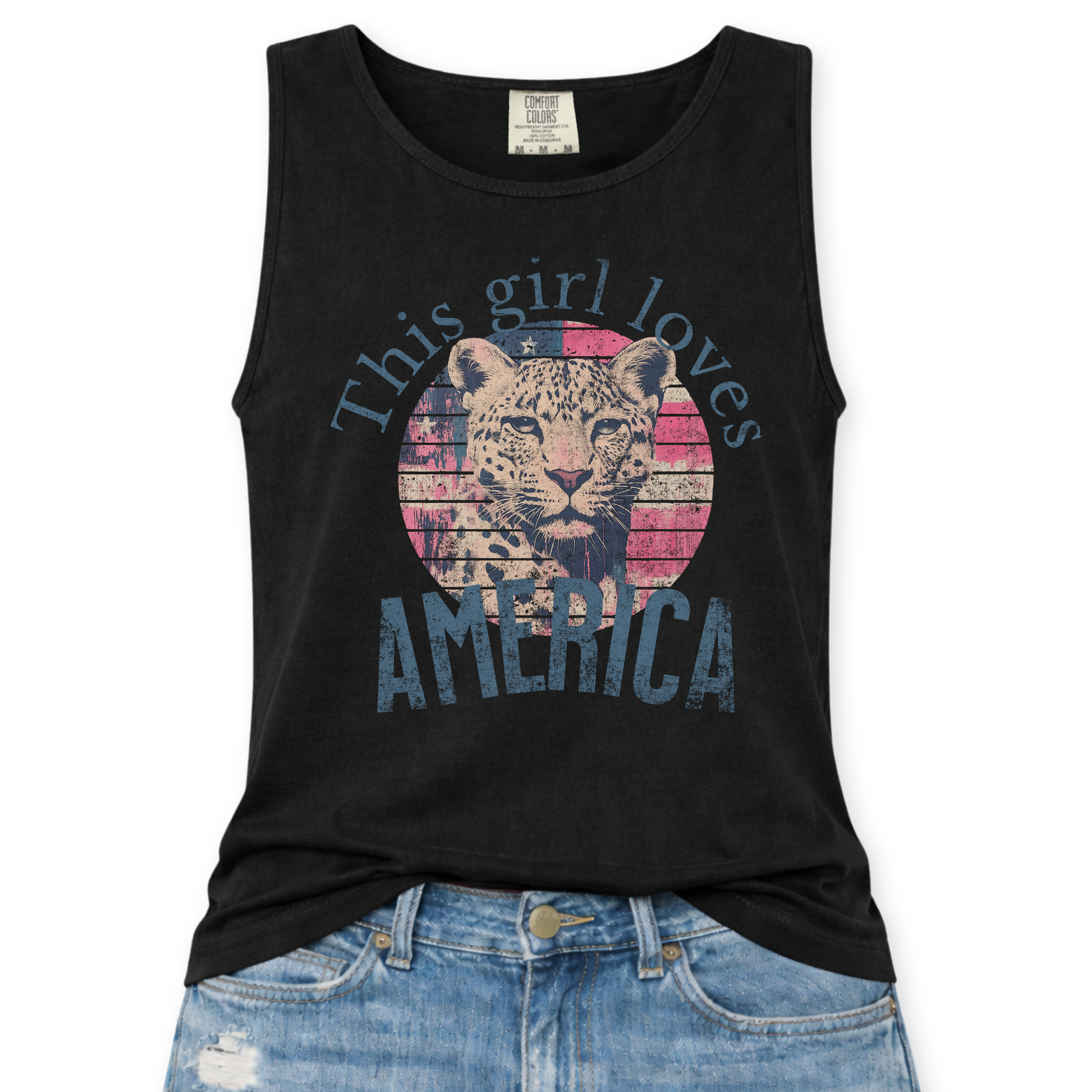 Black Comfort Colors tank top featuring a vintage-style patriotic graphic with a leopard illustration inside a distressed American flag circle and the phrase “This Girl Loves America,” styled with light wash denim jeans.