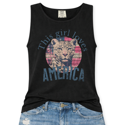 Black Comfort Colors tank top featuring a vintage-style patriotic graphic with a leopard illustration inside a distressed American flag circle and the phrase “This Girl Loves America,” styled with light wash denim jeans.