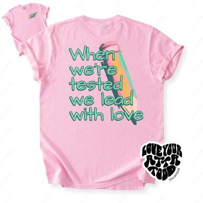 Painted pencil graphic with encouragement text “When We Are Tested We Lead With Love,” thick paint texture and high-contrast color, printed on a Comfort Colors® tee.