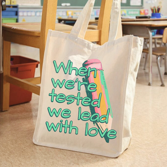 Jumbo canvas tote bag with pencil graphic and “When We Are Tested We Lead With Love” encouragement message, thick paint texture style, Love your ATTA TOOD® brand mark, printed on both sides.