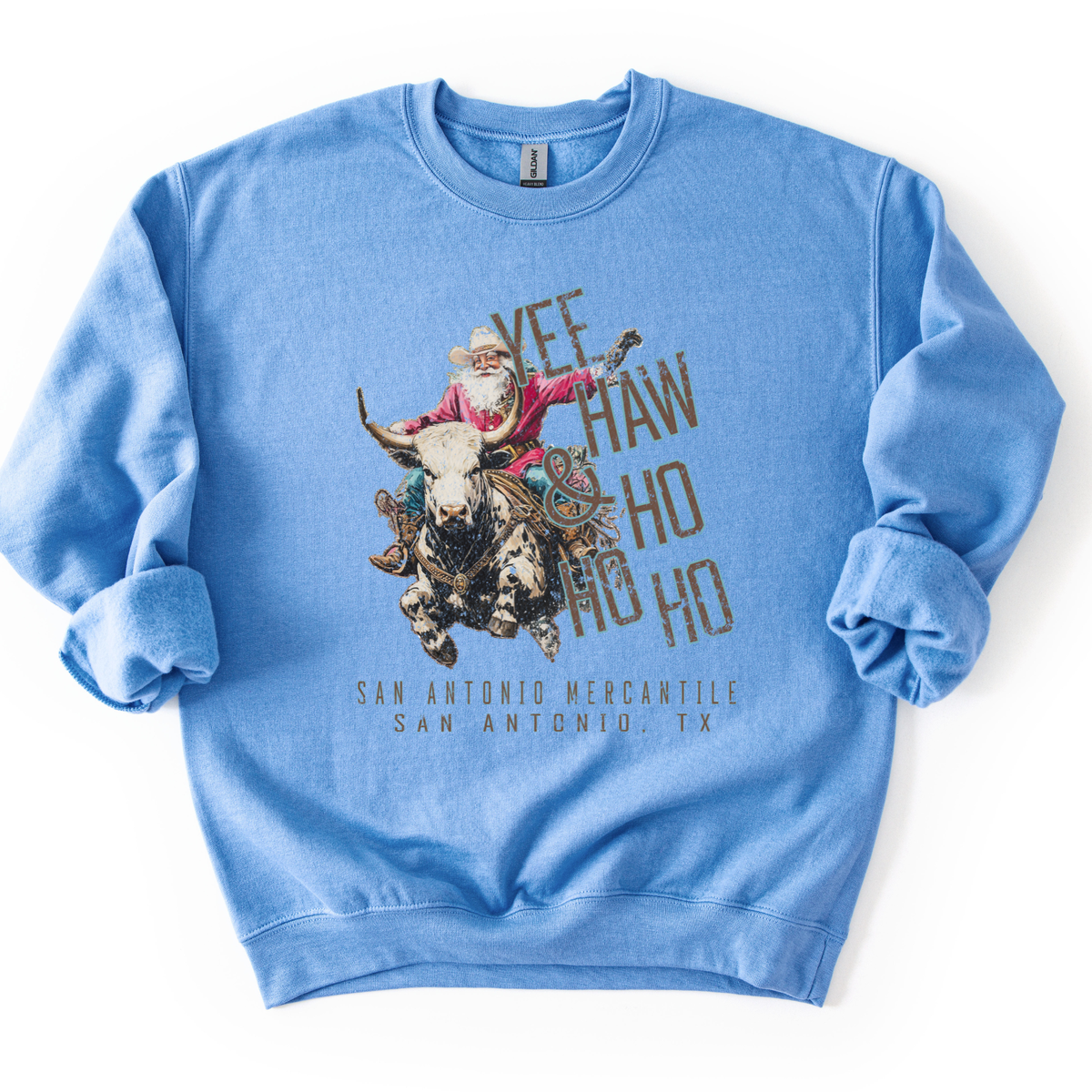 A light blue crewneck sweatshirt featuring a vintage-style graphic of Santa Claus riding a bull with the text 'YEE HO HO HO' and 'SAN ANTONIO MERCANTILE SAN ANTONIO, TX' printed below.